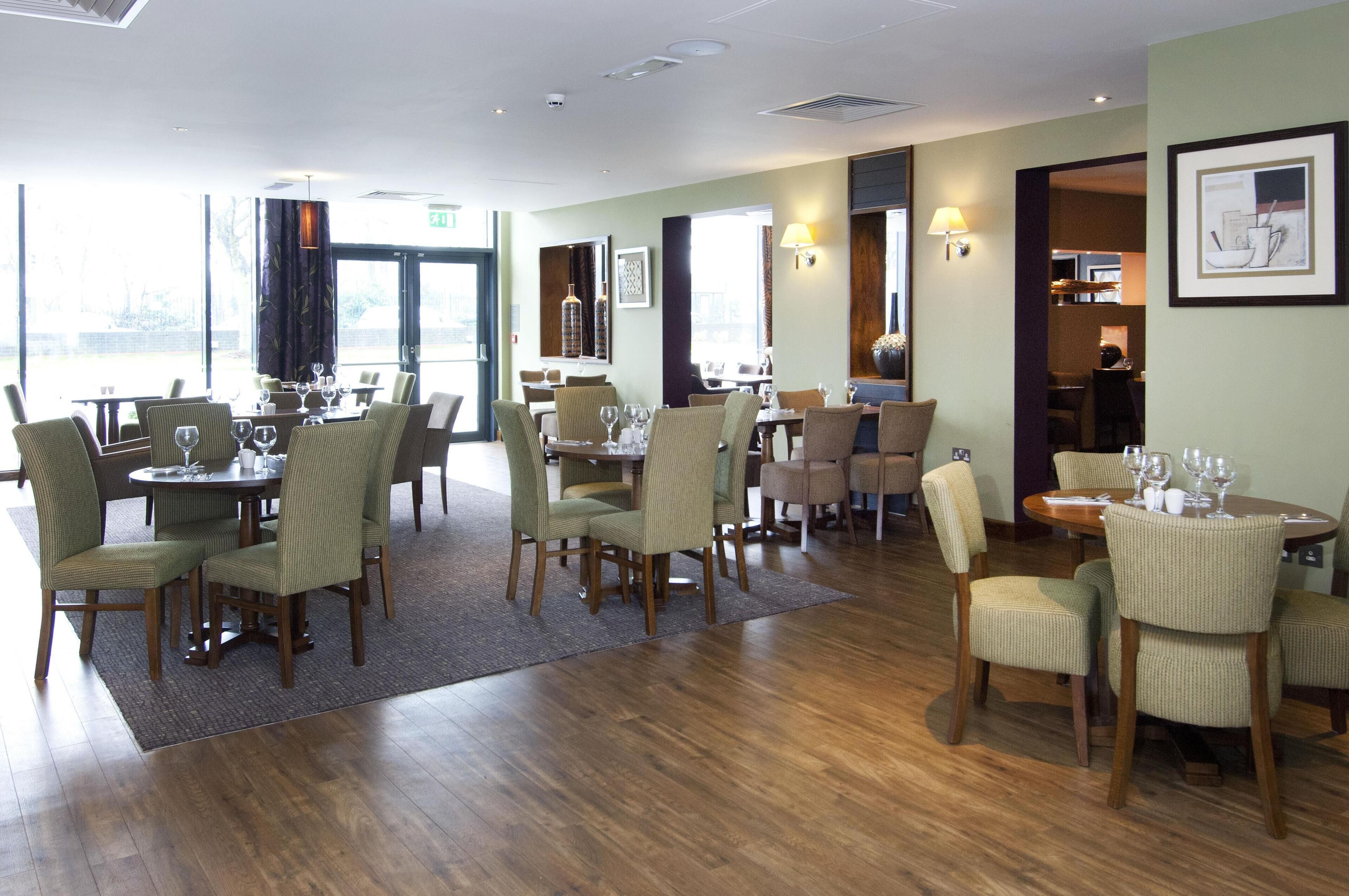 A restaurant with multiple dining tables and chairs, a wooden floor, and a view through the glass doors.