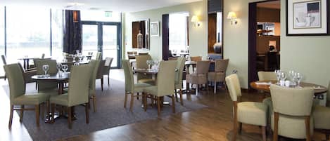 A restaurant with multiple dining tables and chairs, a wooden floor, and a view through the glass doors.