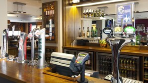 A bar area with multiple beer taps, a cash register, and a selection of bottles and glasses. - Premier Inn Heathrow Airport Terminal 5 (West Drayton)