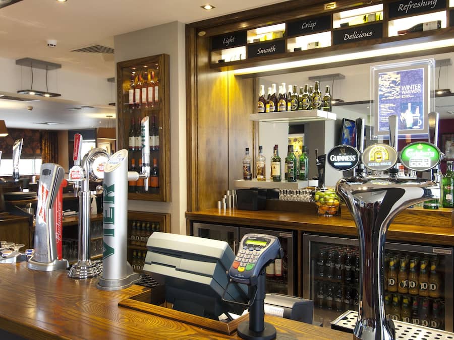 Zona de bar con varias grifos de cerveza, una caja registradora y una selección de botellas y vasos.