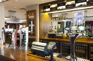 A bar area with multiple beer taps, a cash register, and a selection of bottles and glasses.