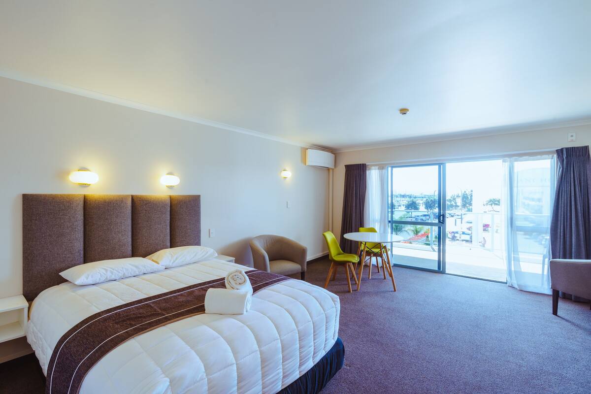 Quarto de hotel com uma cama grande, área de estar com mesa e cadeiras, e vista pela janela.