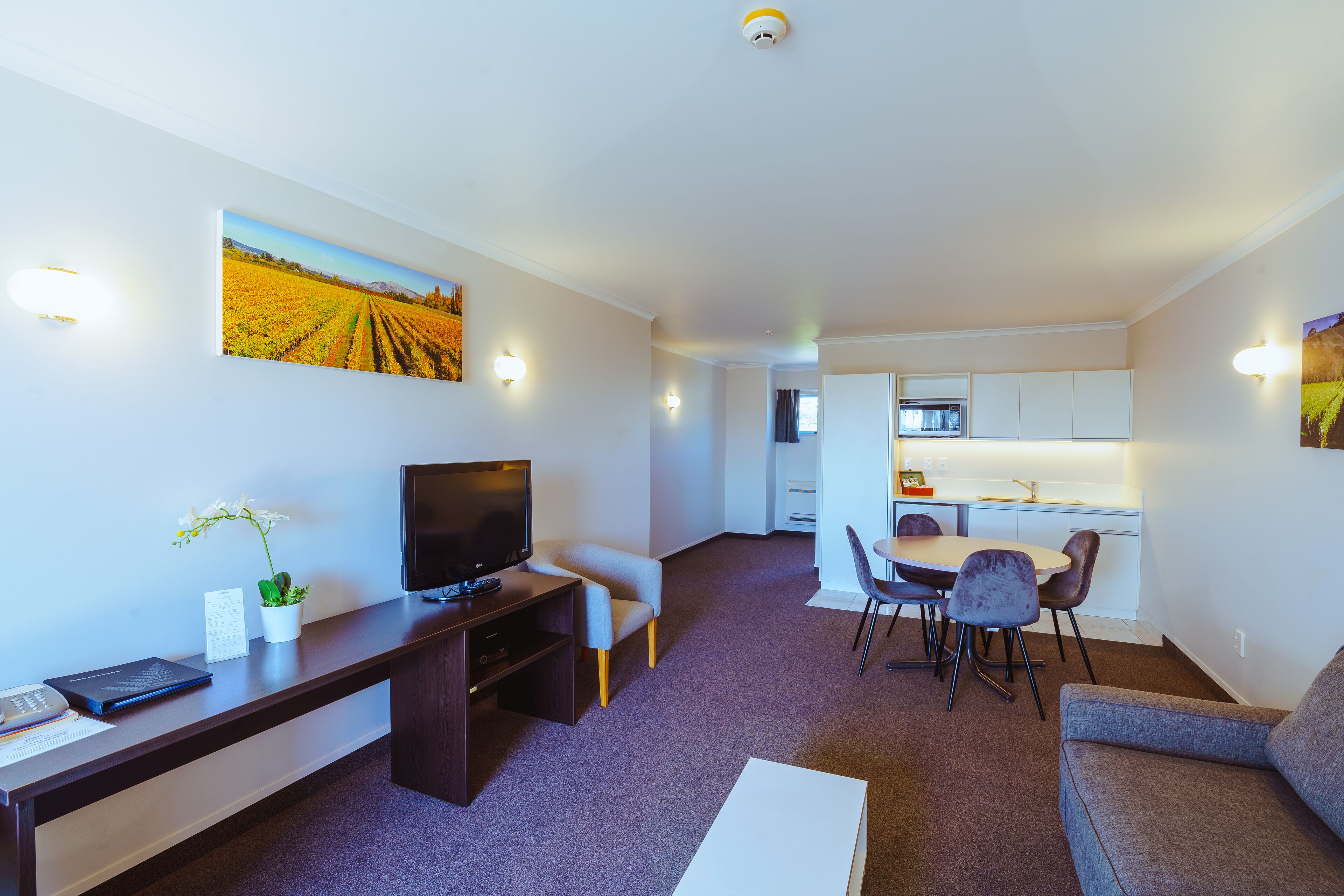 A modern living room with a flat-screen TV, a desk, a sofa, and a dining area with chairs.