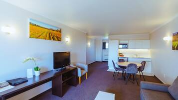 A modern living room with a flat-screen TV, a desk, a sofa, and a dining area with chairs.