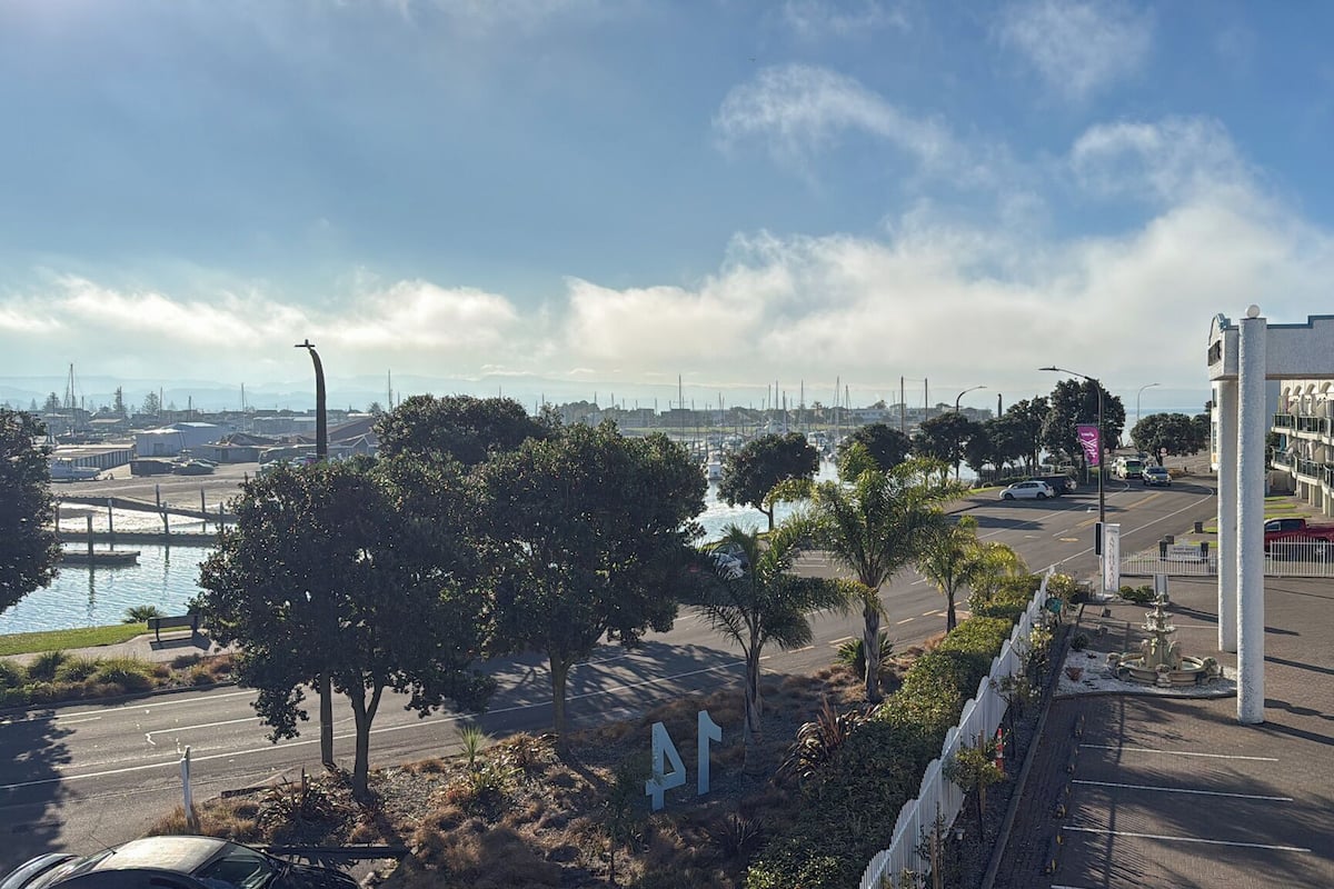 Vista costeira com um porto de iates, uma estrada com cerca branca e um edifício com a placa 'ANCHOR'.