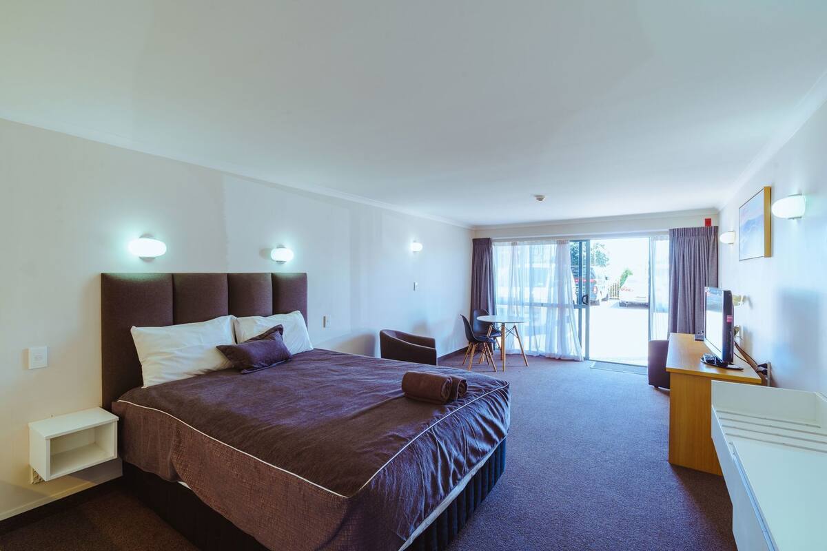 Quarto de hotel com uma cama grande, uma mesa com computador, uma cadeira e vista para o exterior.