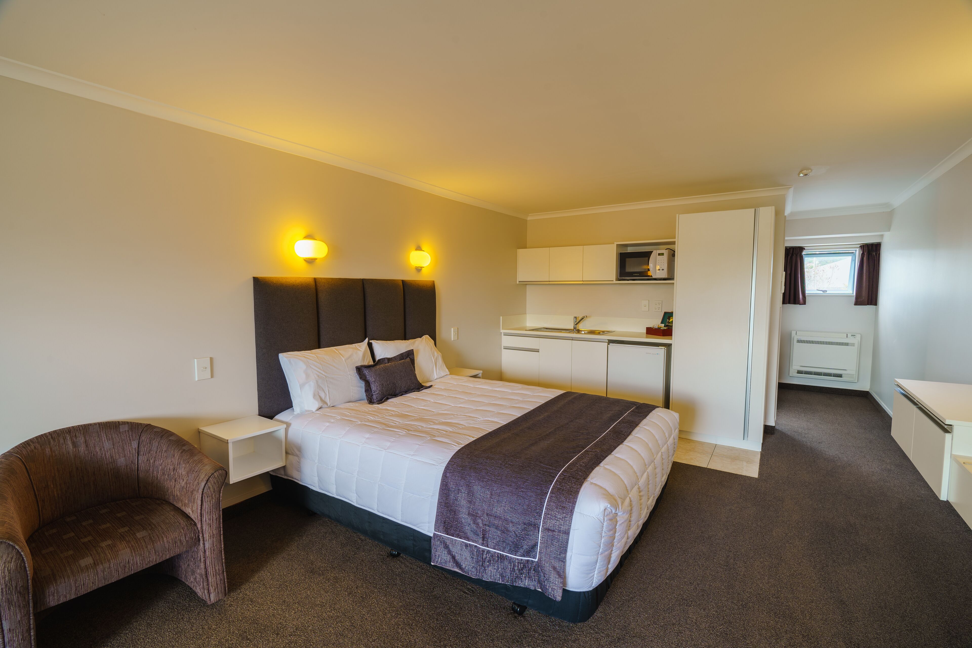 Una habitación de hotel con cama, mesita de noche, silla y kitchenette.