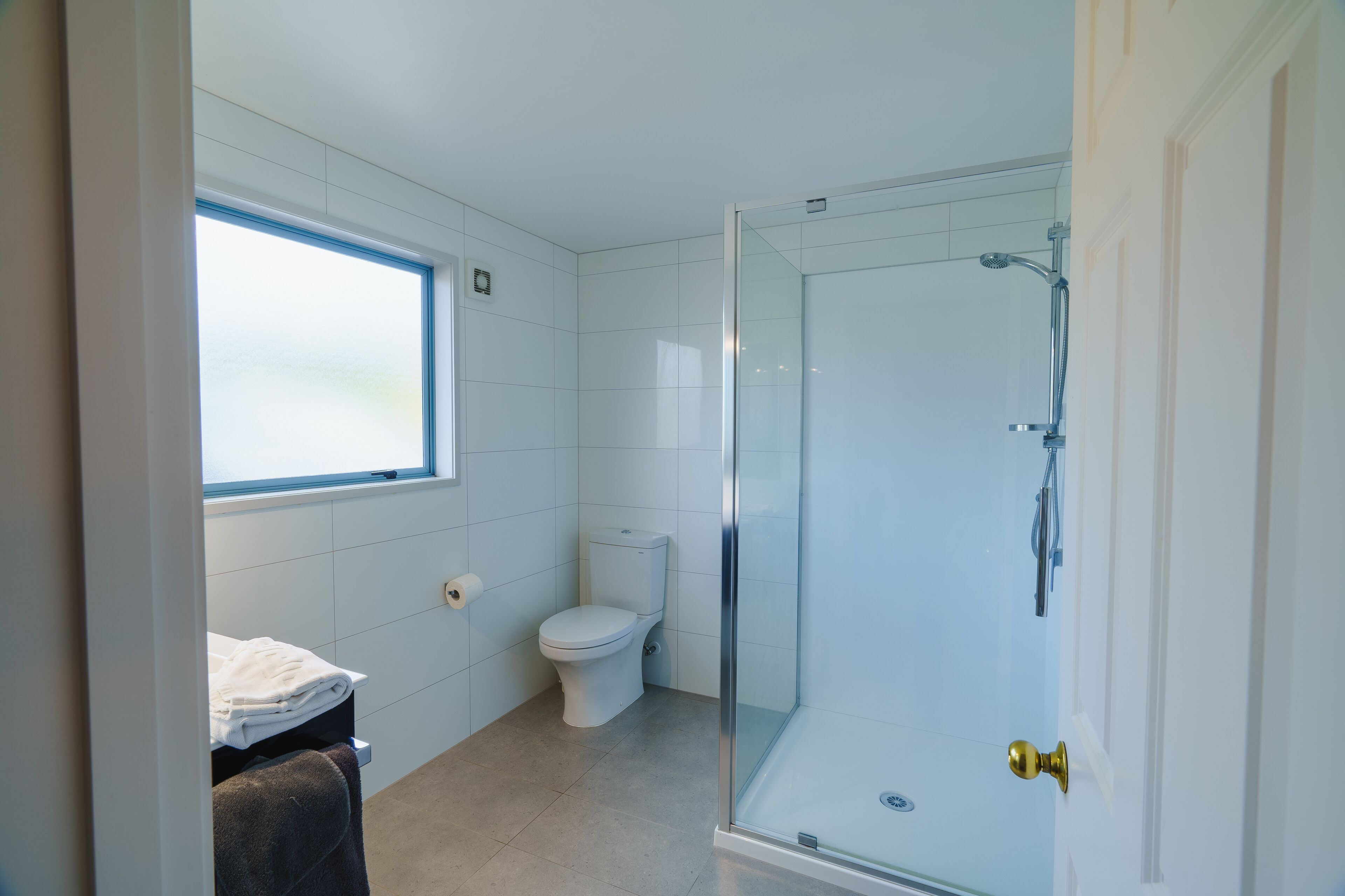 A bathroom with a toilet, a glass shower enclosure, a towel rack, and a window.