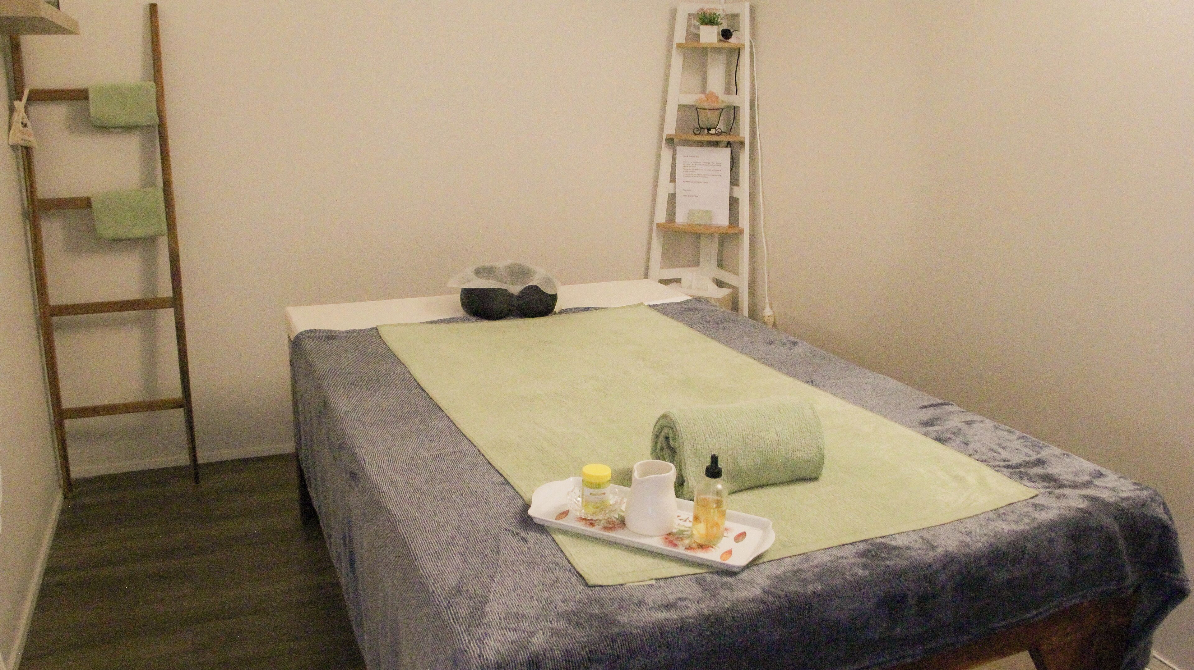 A neatly made bed with a green towel, a tray with toiletries, and a ladder against the wall.