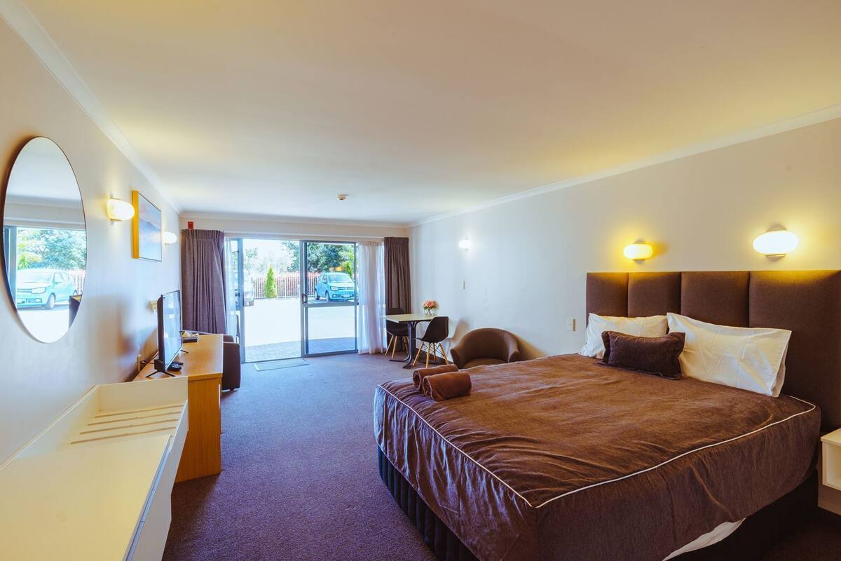 Quarto de hotel com uma cama grande, uma escrivaninha, uma cadeira, um espelho e vista para o exterior.