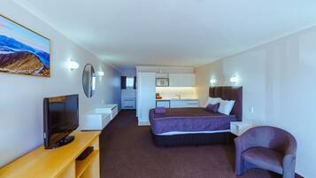 A modern hotel room with a bed, a TV, a desk, a chair, and a bathroom visible in the background.