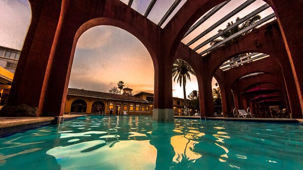 A swimming pool with arched structures, a clear sky, and a building in the background.