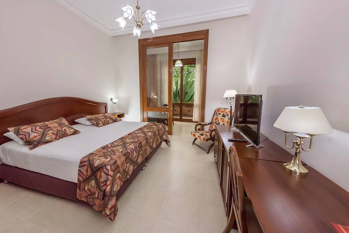 Una habitación de hotel con una cama grande, un escritorio con televisor, una silla y una lámpara.