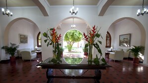 A lobby with a central table, arched doorways, potted plants, and a chandelier.