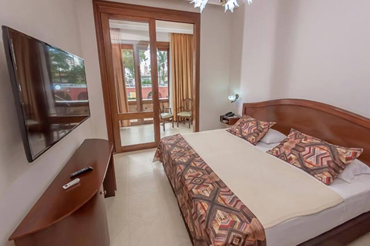 Una habitación de hotel con cama, televisor, escritorio y puerta corrediza a un balcón.