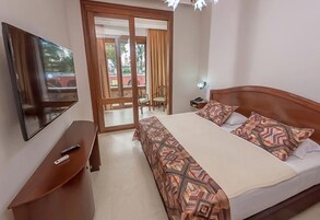 Una habitación de hotel con cama, televisor, escritorio y puerta corrediza a un balcón.