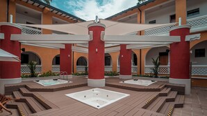 A rooftop pool area with two hot tubs, wooden deck, and a covered seating area.