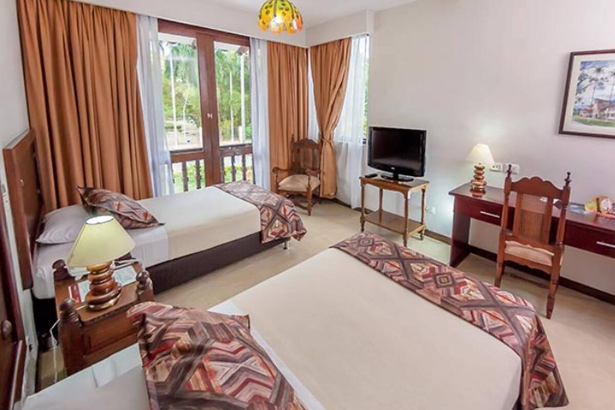 Habitación de hotel con dos camas, televisión, escritorio con lámpara y una silla.