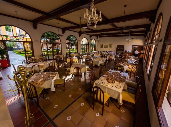 A restaurant with multiple tables and chairs, large windows, and a chandelier. - Hotel Guadalajara (Guadalajara de Buga)