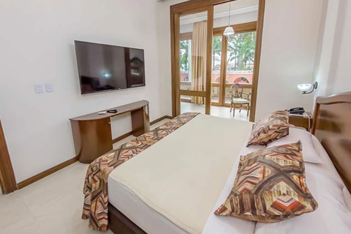 Habitación de hotel con cama, televisión, escritorio y balcón con vistas.