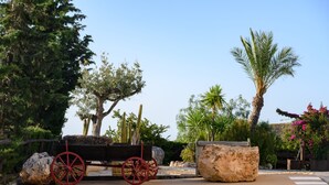A rustic outdoor setting with a wooden cart, large rocks, and various trees including a palm. - Sol de Taberno (Taberno)