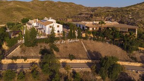 A white building with multiple windows and a flat roof, surrounded by greenery and hills. - Sol de Taberno (Taberno)