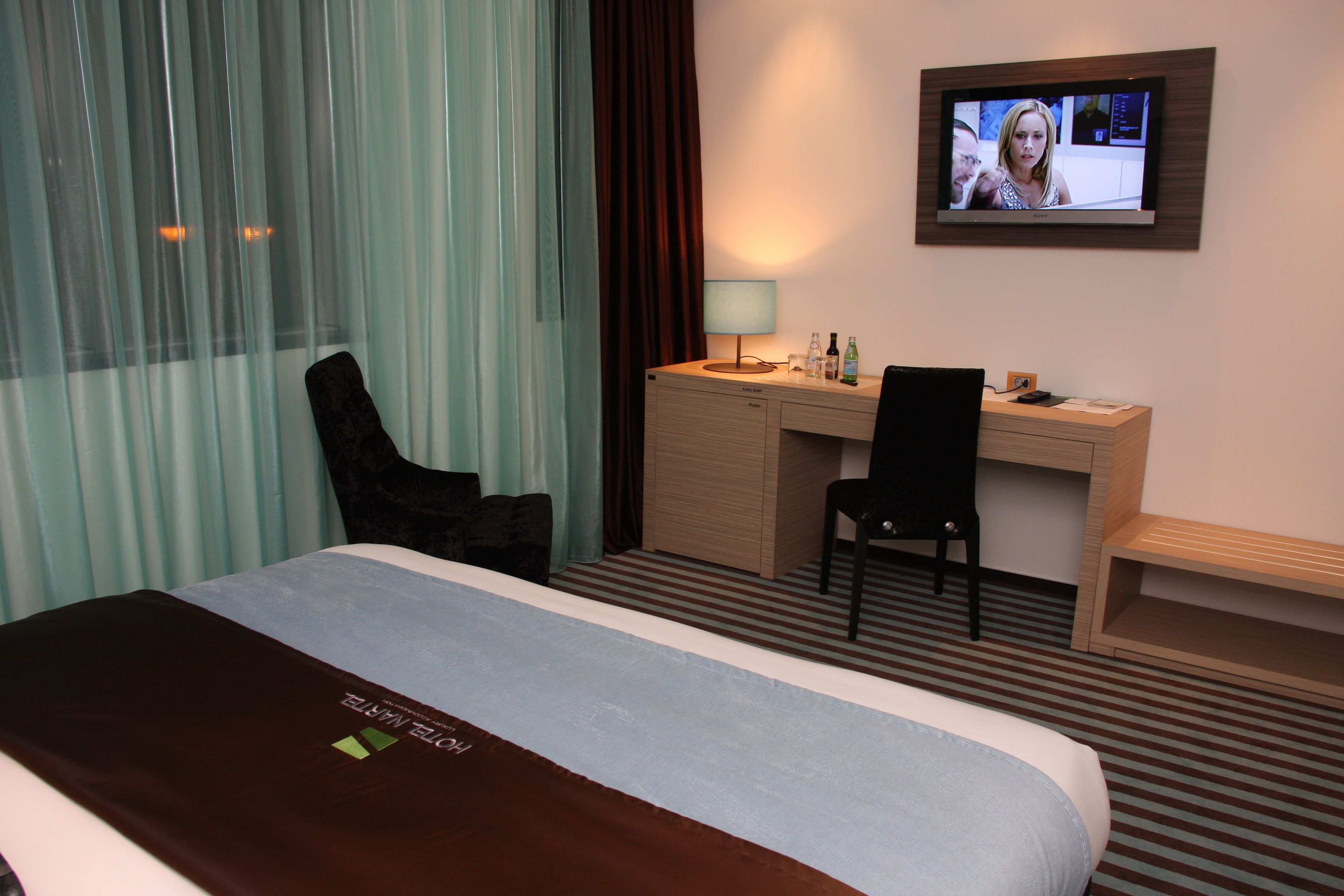 Une chambre d’hôtel équipée d’un lit, d’un bureau, d’une chaise, d’une télévision et d’une fenêtre avec des rideaux.