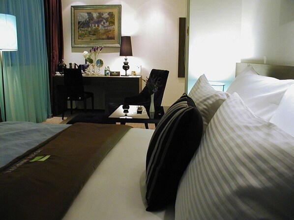 A hotel room with two beds, a desk, a chair, and a painting on the wall. - Nartel Hotel (Pristina)
