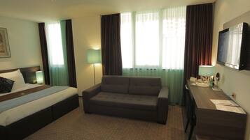Una habitación de hotel con cama, sofá, escritorio y televisión.
