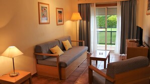 A cozy living room with a sofa, two lamps, a TV, and a balcony with curtains. - Alagoa Azul Apartments (Castro Marim)