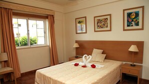 A hotel room with a large bed, two bedside tables, a window with curtains, and three framed artworks on the wall. - Alagoa Azul Apartments (Castro Marim)