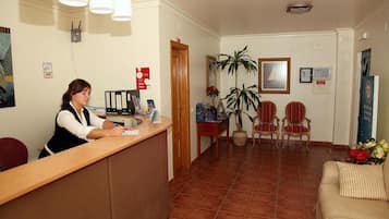 A reception area with a receptionist, a wooden reception desk, a potted plant, two armchairs, and a sofa.