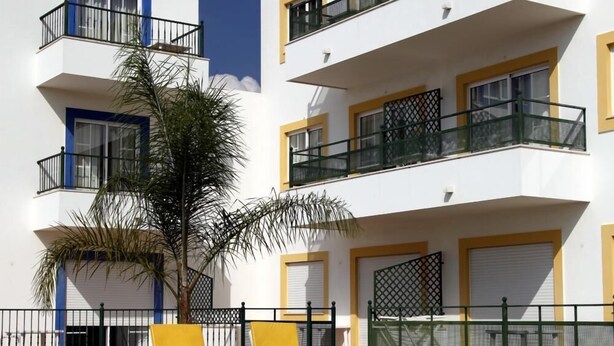 A swimming pool with two sun loungers, a palm tree, and a building with balconies and windows. - Alagoa Azul Apartments (Castro Marim)