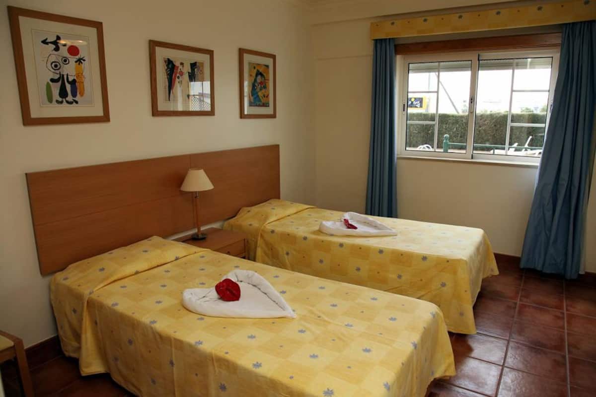 A hotel room with two beds, a wooden headboard, and three framed artworks on the wall.