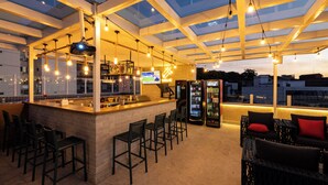 An outdoor bar area with a high ceiling, bar stools, seating, and a TV screen. - Arosa Rio Hotel (Rio de Janeiro)