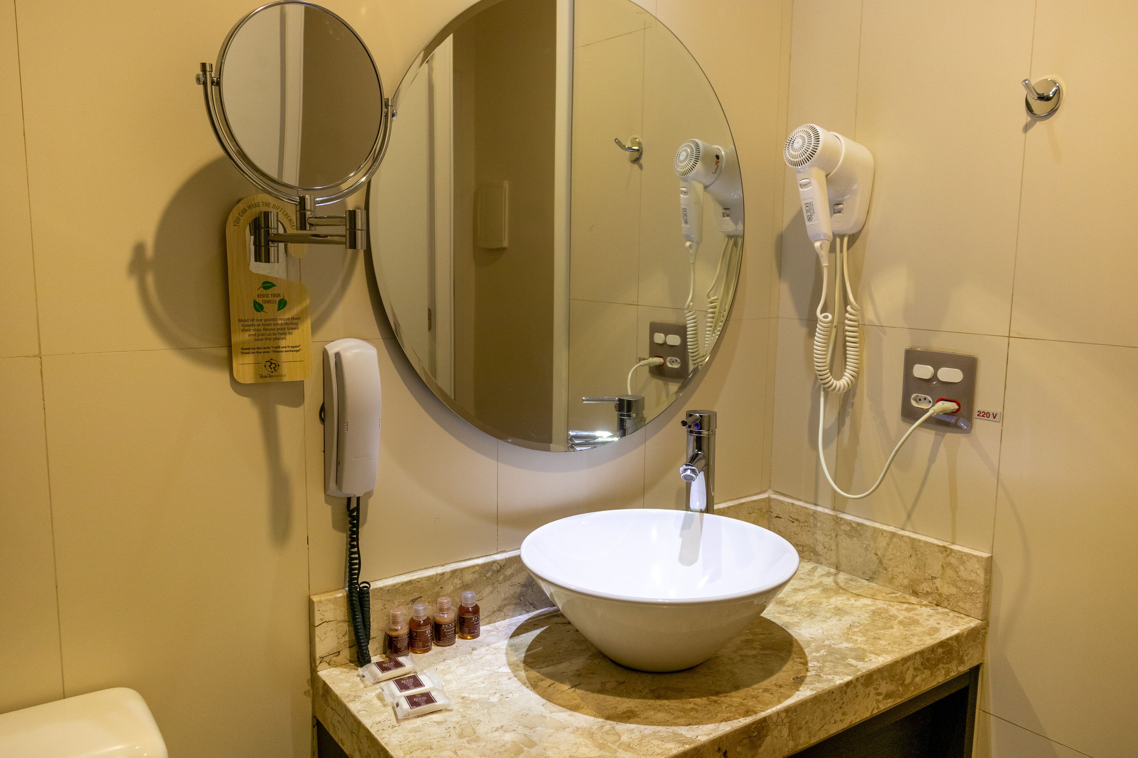 A bathroom with a round mirror, a sink with a large basin, a hairdryer, and a hand dryer.