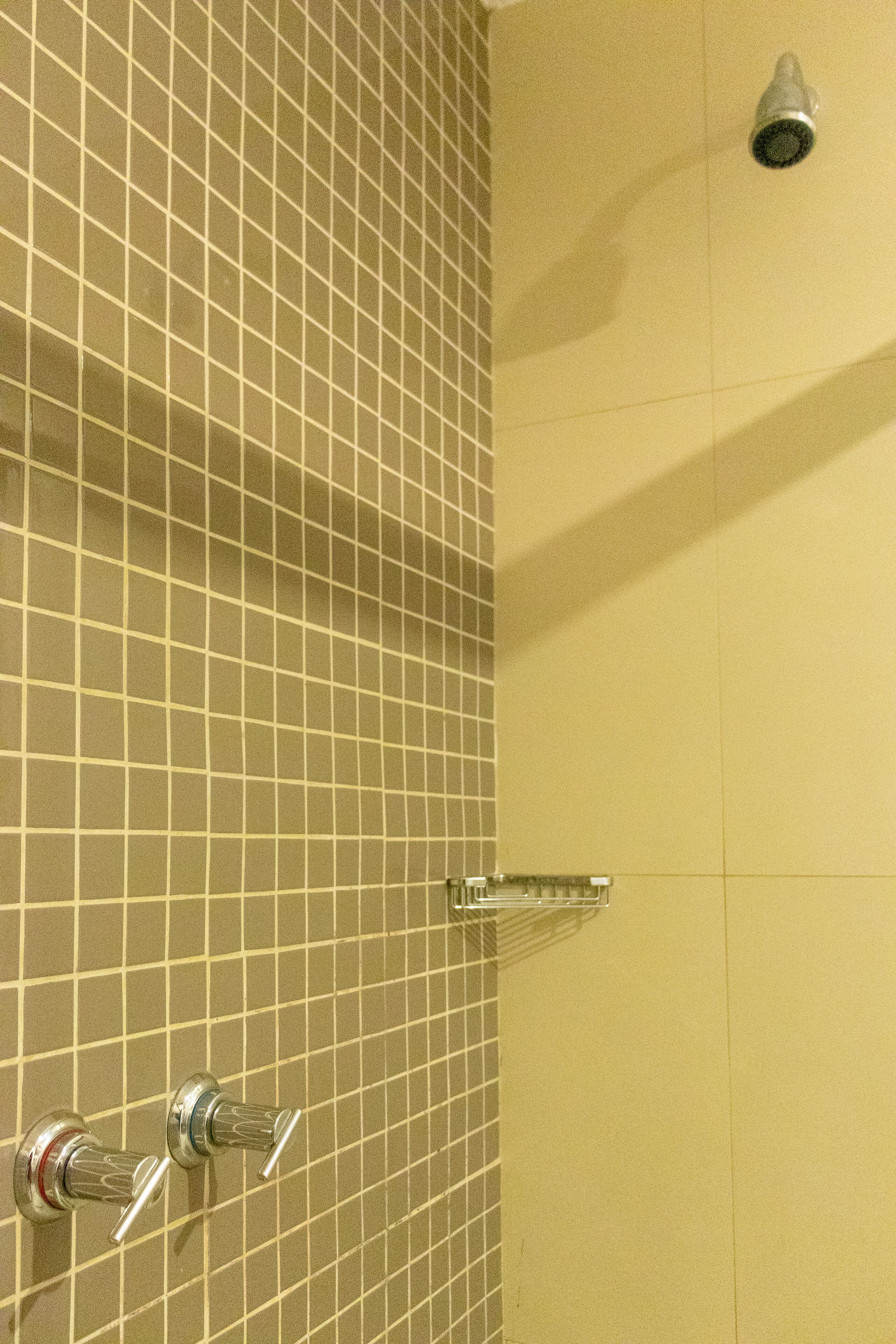 A tiled shower wall with a handheld showerhead and a wall-mounted faucet.