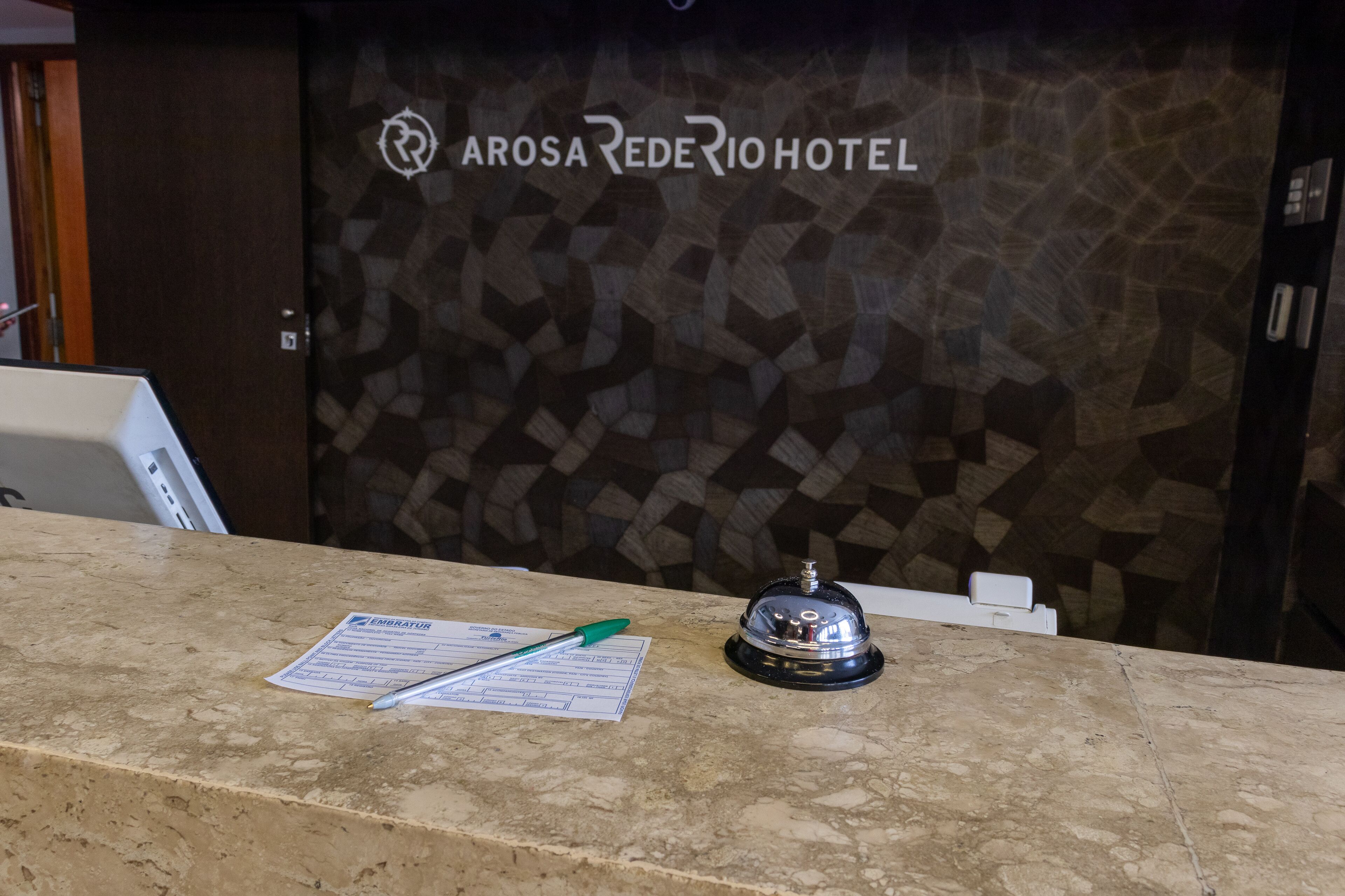 A reception desk with a check-in form, a pen, and a bell at the Arosá Rede Rio Hotel.