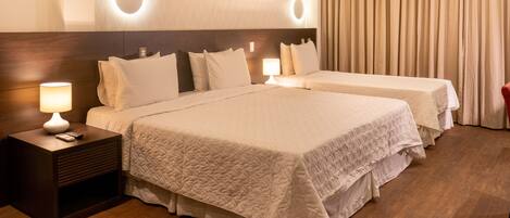 A hotel room with two beds, a nightstand with a lamp, and a wall-mounted light fixture.