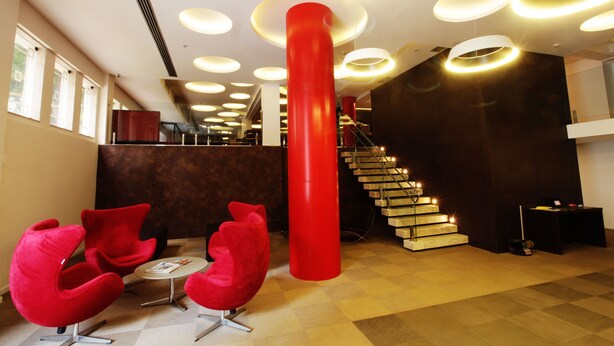 A modern lobby with a staircase, red chairs, and a large red pillar. - Arosa Rio Hotel (Rio de Janeiro)