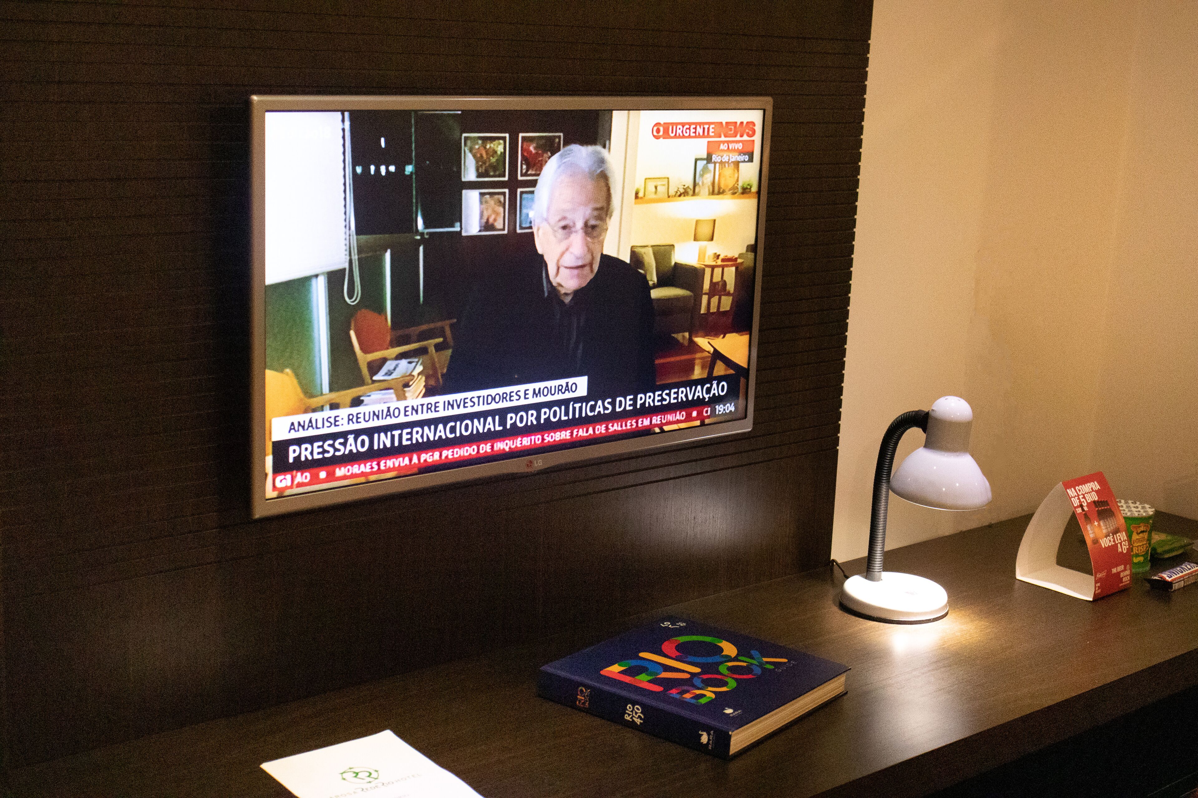Un téléviseur diffusant un journal télévisé, un bureau avec une lampe, un livre et une boîte de mouchoirs.