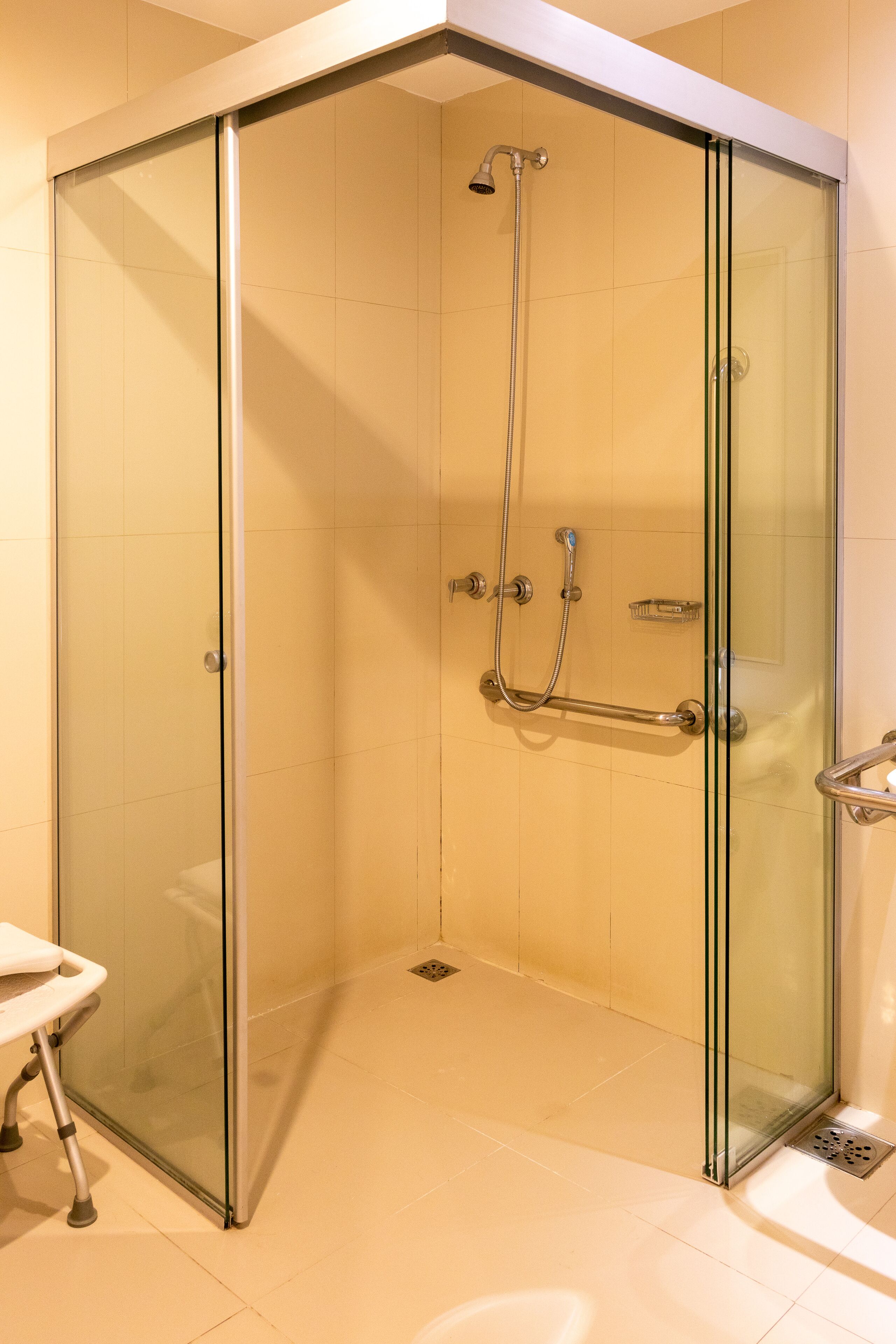 A glass-enclosed shower stall with a handheld showerhead and a handheld shower attachment.