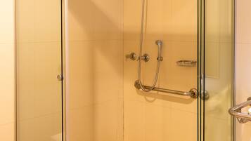 A glass-enclosed shower stall with a handheld showerhead and a handheld shower attachment.