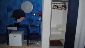 A bathroom with a blue wall, a round mirror, a small sink, a chair, a white cabinet, and a towel rack. - Karmik Concept Apartments (Rhodes)