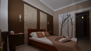 A modern bedroom with a large bed, a nightstand, a wall-mounted lamp, and a door leading to another room. - Karmik Concept Apartments (Rhodes)