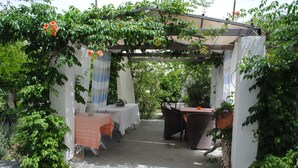A covered outdoor seating area with tables and chairs, surrounded by greenery and a pergola structure. - Karmik Concept Apartments (Rhodes)