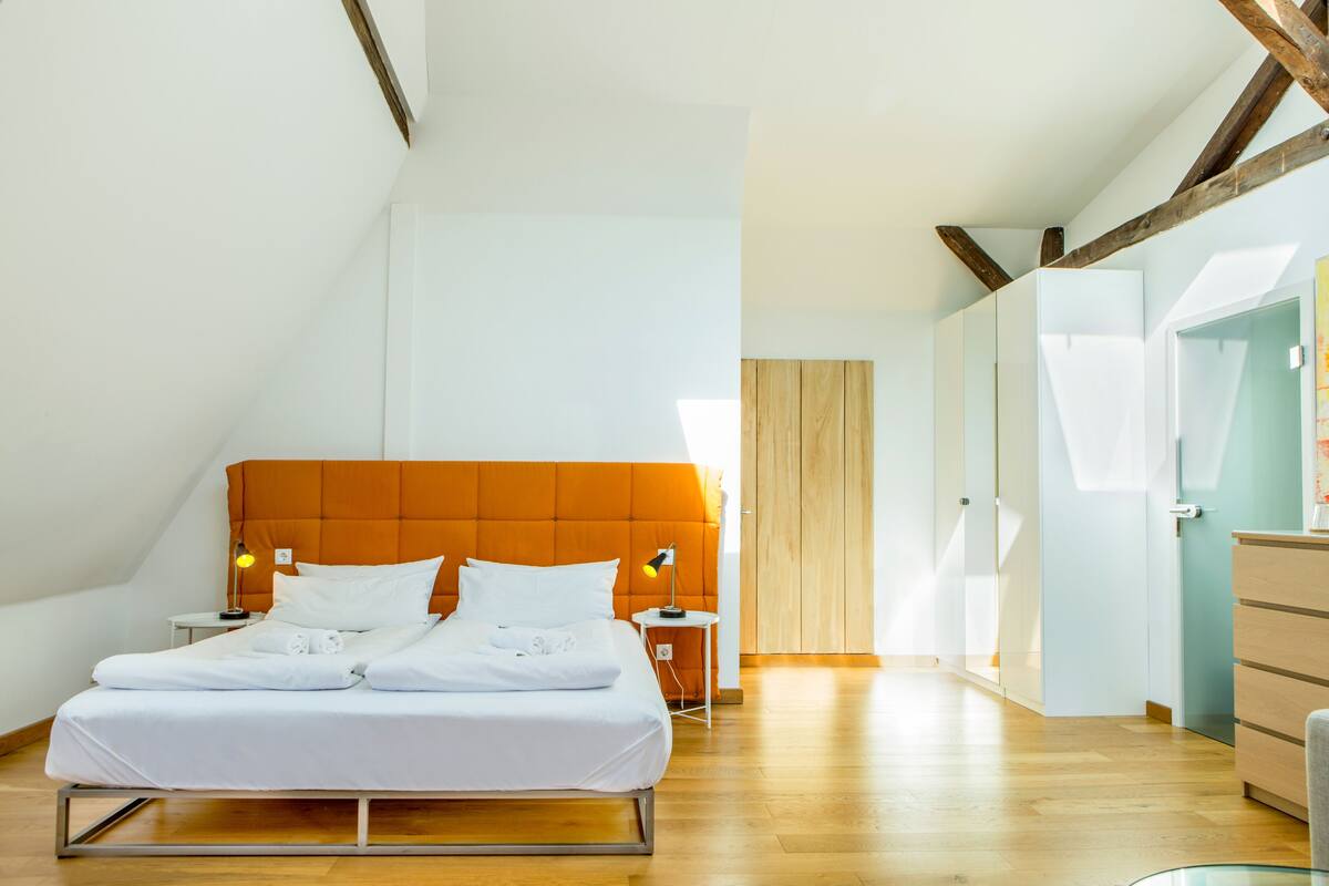 A modern bedroom with a large bed, wooden beams, a small bedside table, and a nightstand.
