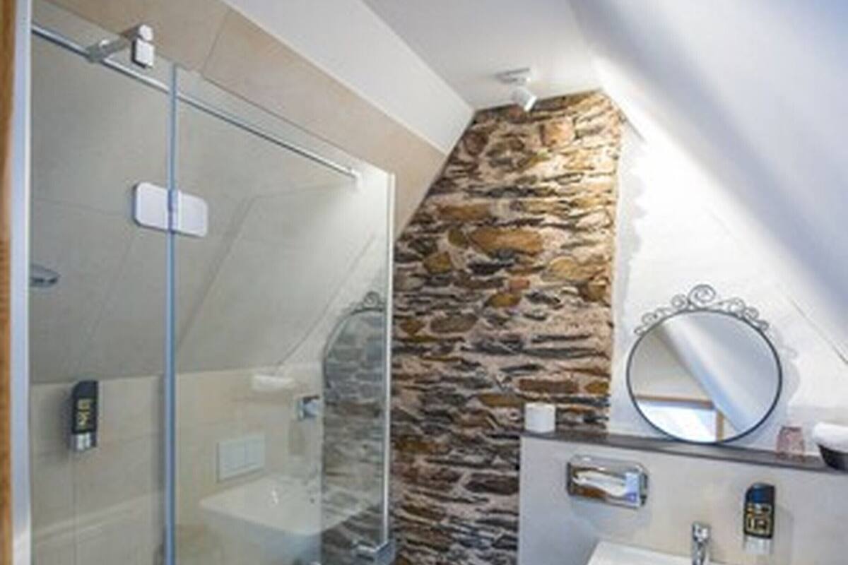 A modern bathroom with a glass shower enclosure, a stone accent wall, and a white sink with a mirror.