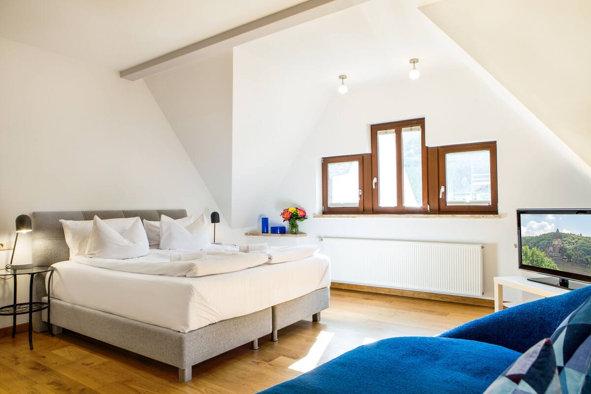 A bedroom with a bed, a TV, a window, and a radiator.