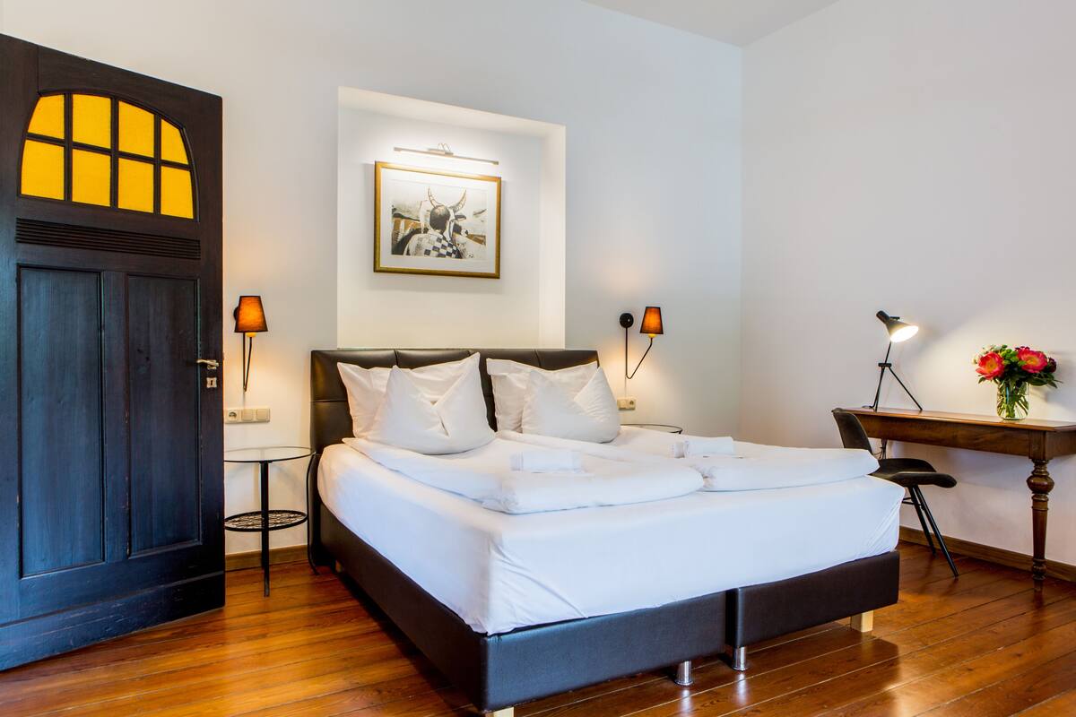 A neatly made bed with white linens, a dark wooden headboard, and two bedside lamps.